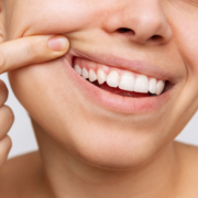 Gros plan sur un visage souriant avec une personne qui tire doucement sur sa joue pour montrer des dents blanches et des gencives saines.